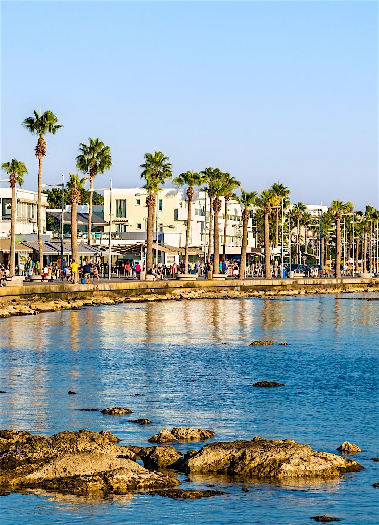 Paphos waterfront promenade with palm trees, seaside cafés, coastal walkway and Mediterranean Sea views in Cyprus.