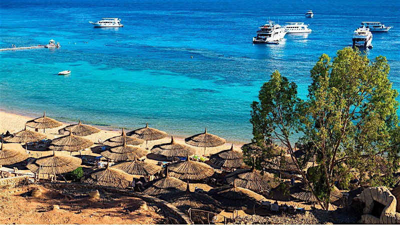 Sharm El Sheikh Egypt beach with turquoise Red Sea waters, sun umbrellas and luxury boats