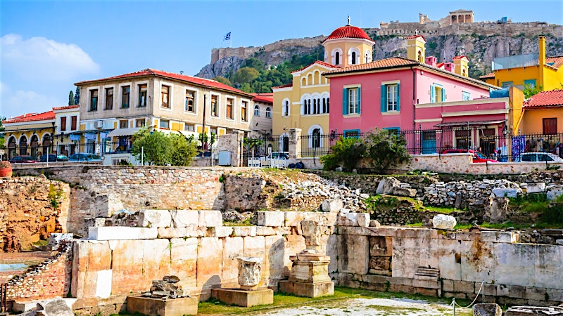 Ancient Roman Agora ruins with colorful Plaka buildings and Acropolis hill, Athens, Greece.