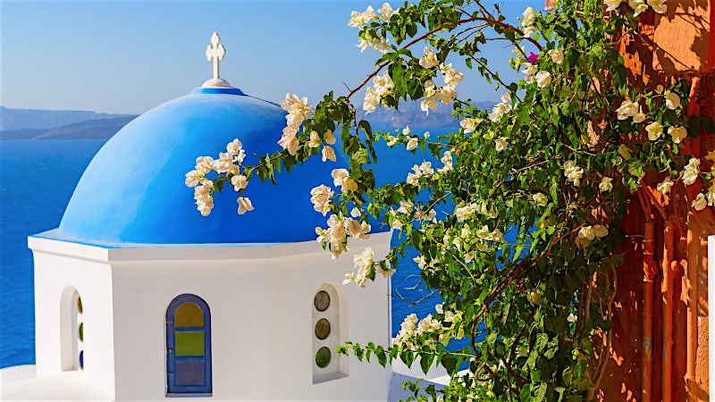 Blue-domed church with bougainvillea overlooking the Aegean Sea, Santorini, Greece.