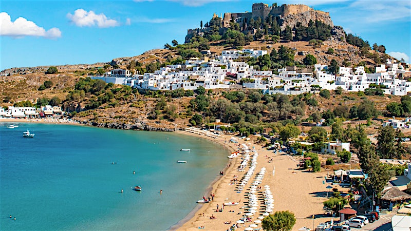 Lindos Beach with whitewashed village and Acropolis hilltop ruins, Rhodes, Greece.