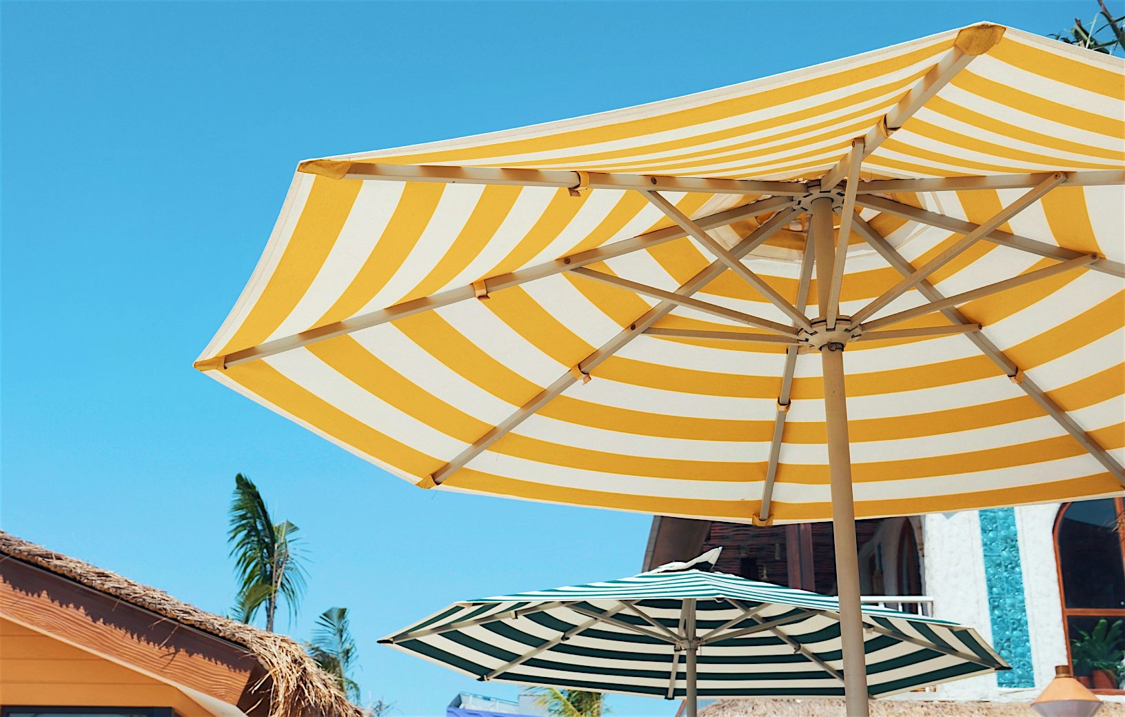 Bright yellow and white beach umbrella at a tropical-style resort, capturing the sunshine and relaxation of Summer 2026 holidays by Sundeals.