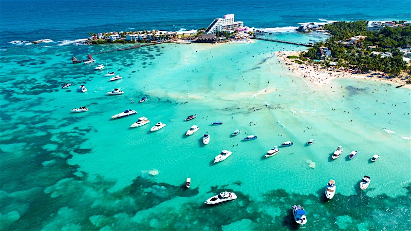 Aerial view of Playa Mujeres turquoise lagoon, luxury resorts and boats, Cancun, Mexico.