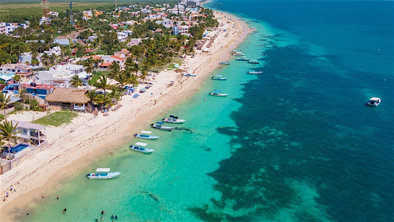 Aerial view of Puerto Morelos beach with turquoise Caribbean Sea, anchored boats and palm-lined coastline, Mexico.