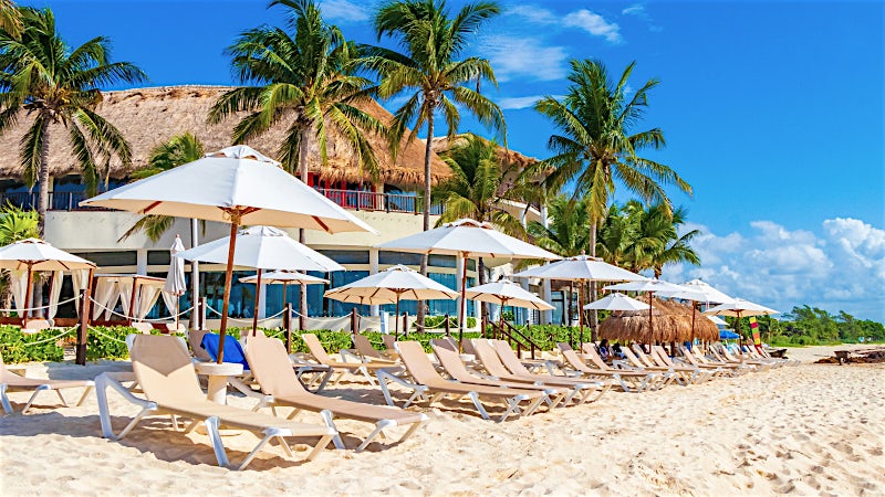 Beachfront resort with sun loungers, palm trees and white sand coastline, Playa del Carmen, Mexico.