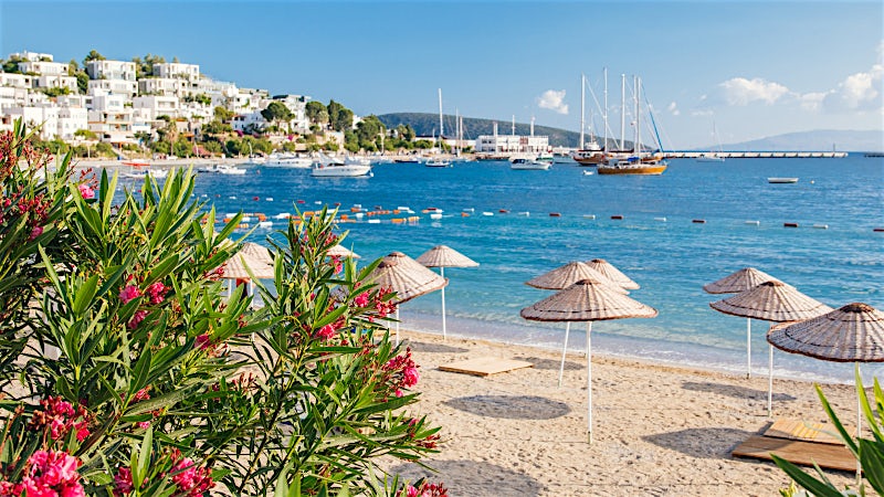 Bodrum Turkey beach with turquoise sea, parasols, yachts and whitewashed hillside buildings
