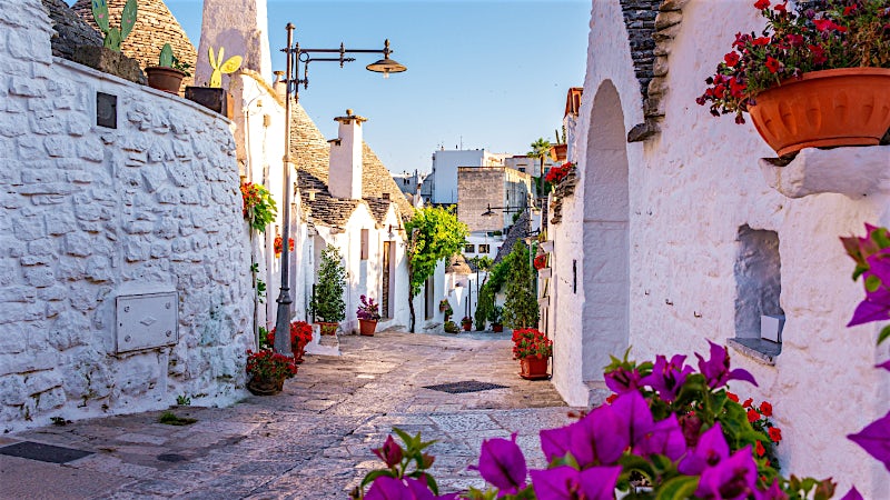 Puglia Italy whitewashed village street with traditional trulli houses and colourful flowers