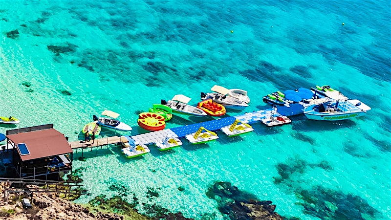 Makronissos Beach lagoon with crystal-clear water, boats and floating pontoons, Cyprus.