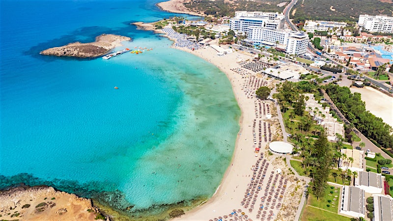 Aerial view of Nissi Beach with turquoise lagoon, golden sand and beachfront resorts, Ayia Napa, Cyprus.