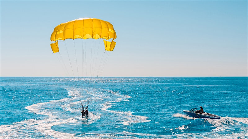 Parasailing adventure over turquoise sea with speedboat towing riders on a sunny coastal day.