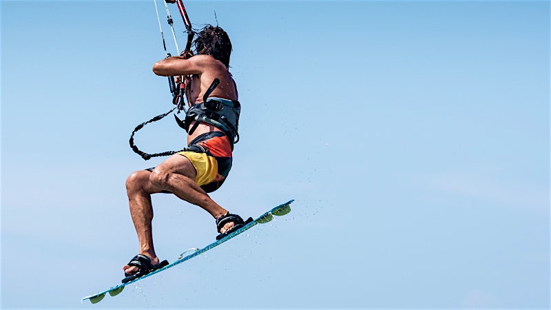 Kitesurfer performing an aerial jump over the ocean during a watersports adventure.