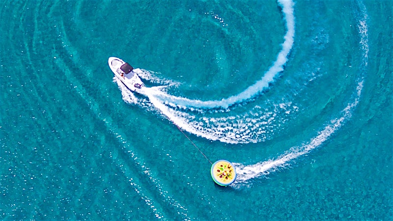Speedboat towing an inflatable water ride across crystal-clear Mediterranean sea in Greece.