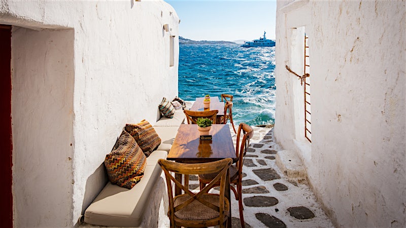 Seafront restaurant terrace in Mykonos with whitewashed architecture and Aegean Sea views.