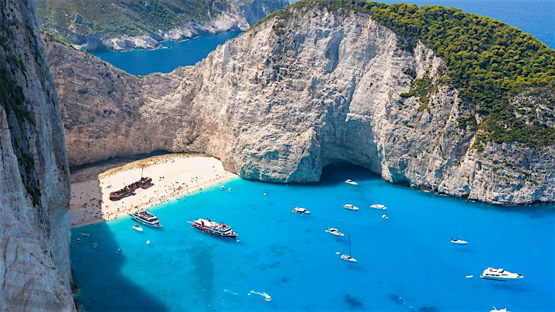 Navagio Beach in Zakynthos with turquoise waters, limestone cliffs and boats.
