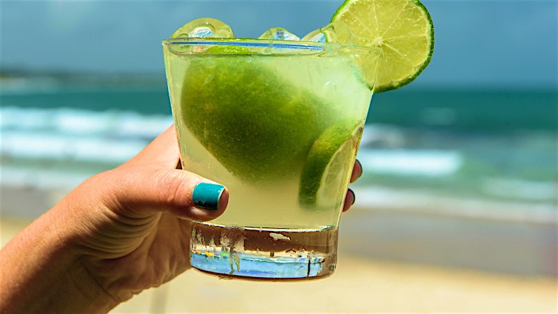 Fresh caipirinha cocktail with lime and ice served on a sunny beach.