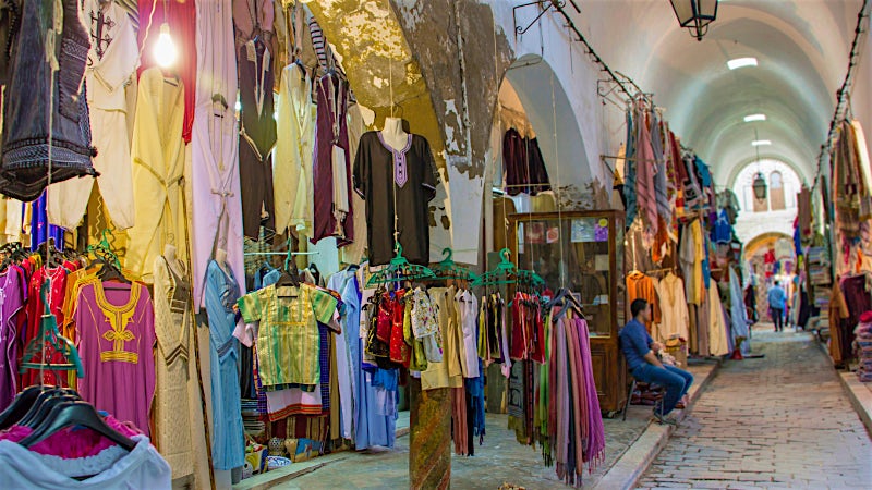 Traditional Tunisian souk with colourful clothing stalls and historic market architecture.