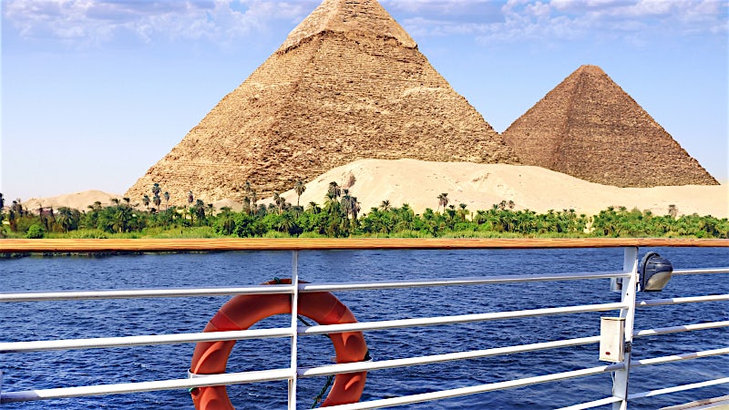 Nile River cruise passing the Pyramids of Giza with palm-lined riverbanks in Egypt.