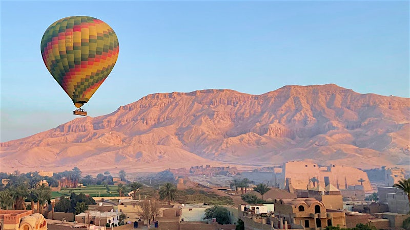 Hot air balloon floating above Luxor's desert landscape and ancient Egyptian landmarks.