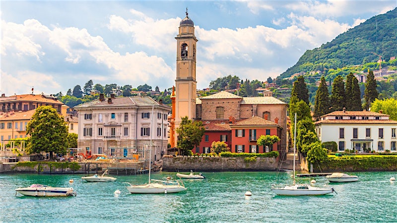 Lakefront village with church bell tower, boats and mountain scenery, Lake Como, Italy.