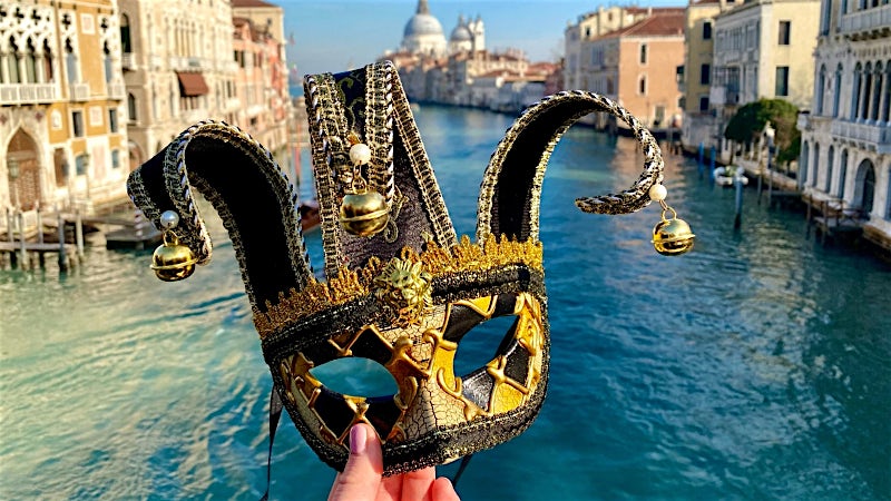 Venetian carnival mask overlooking the Grand Canal and historic waterfront, Venice, Italy.