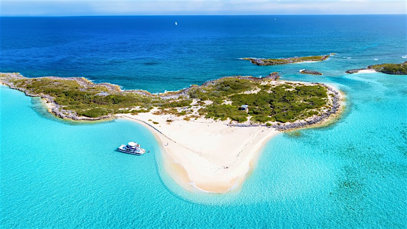 Aerial view of Bahamas sandbar island with crystal-clear turquoise water and anchored boat.