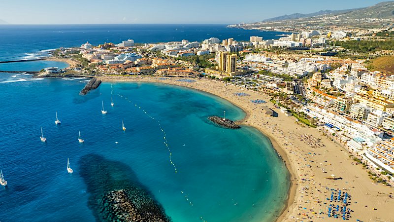 Golden sands and calm turquoise waters curve around Los Cristianos beach, a popular setting for sunny Tenerife Value holidays.