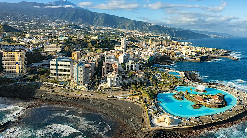 Aerial view of Puerto de la Cruz with coastal pools, oceanfront hotels and volcanic landscapes, ideal for Tenerife Value holidays.