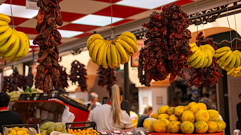 Fresh fruit and hanging red peppers fill a Tenerife market stall, highlighting authentic shopping experiences on Value holidays.