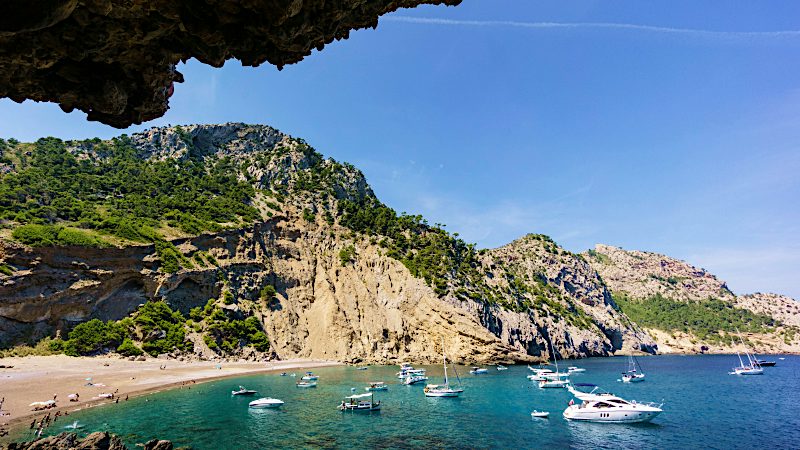 Alcúdia cove with turquoise sea, yachts, sandy beach and dramatic Mallorca cliffs.
