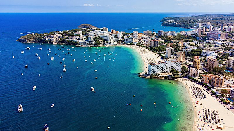 Aerial view of Magaluf beach, turquoise bay, beachfront hotels and boats in Mallorca.