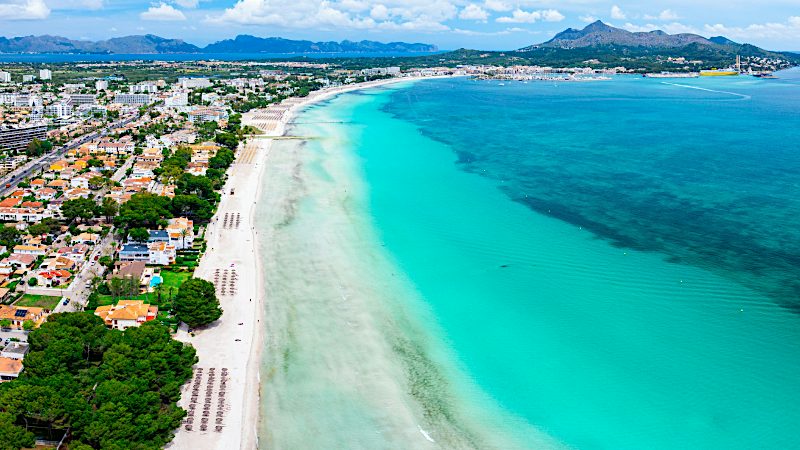 erial view of Playa de Muro beach with white sand, turquoise sea and Mallorca mountains.