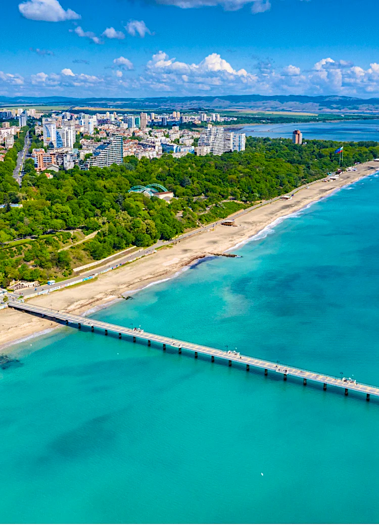 Aerial view of Burgas coastline, Bulgaria, featuring a long seaside pier, sandy beach, Black Sea shoreline, Sea Garden park and modern city skyline.