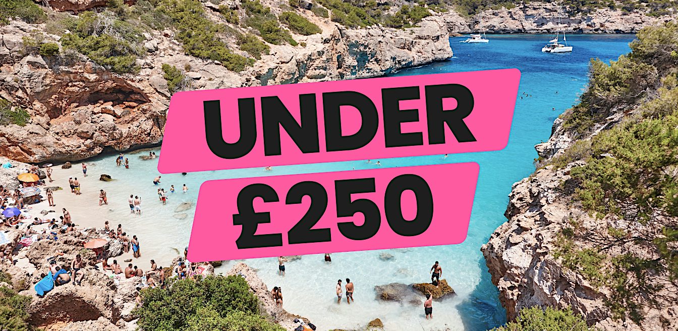 Turquoise cove and sandy beach framed by pine-covered cliffs, showcasing Value holidays and affordable seaside escapes under £250.
